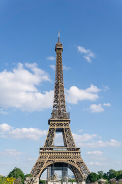 Photograph of the eiffel tower on a sunny day in portrait format with blue sky and white clouds.