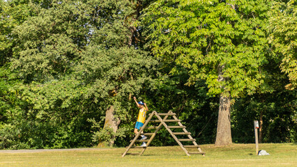 Obraz na płótnie Canvas Young man from behind climbing a wooden obstacle in a green park