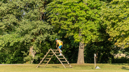Young man from behind climbing a wooden obstacle in a green park