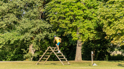 Young man from behind climbing a wooden obstacle in a green park