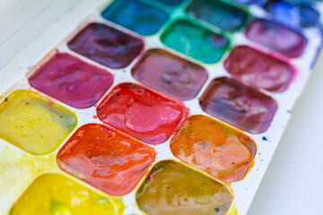 Palette with used watercolors, bright multi-colored paints, side view, selective focus