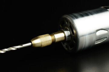 Electric micro drill for drilling of printed circuit boards (PCB). Small drilling machine made of steel. DC brushed motor. Selective focus. Isolated on black background.