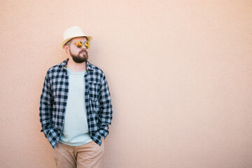 Handsome caucasian man wearing summer hat and plaid shirt smiling happy near wall with copy space - travel vacations and summer holiday concept