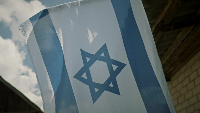 Blue and white flag of Israel waving on the background of a blue cloudy sky