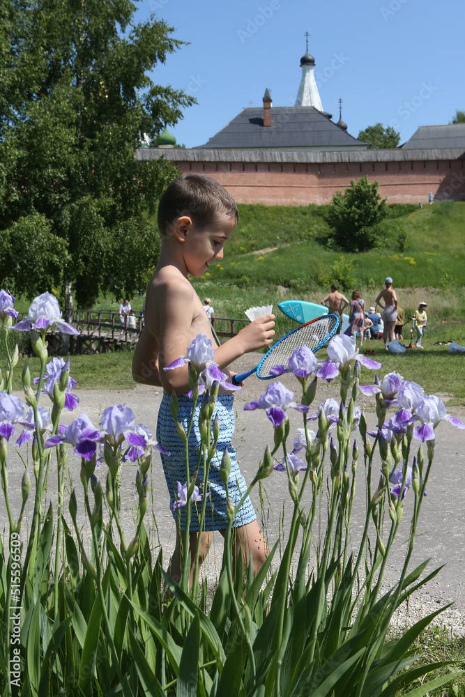 Wall mural Happy child and iris flowers in Suzdal town, Russia. Russian tourist kid, toddler on vacation in country. Domestic tourism, travel. Kremlin in Suzdal, Vladimir region, Russia. Summer garden, nature