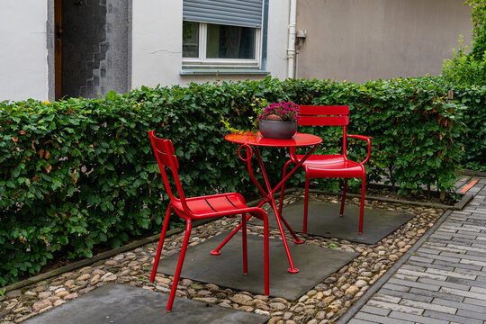 Two metal chairs and a table painted with red paint in the courtyard of the house.