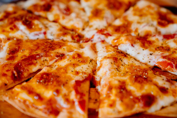 toasted cheese pizza cut into pieces on a wooden round cutting board. traditional treats for the party. Italian cuisine.