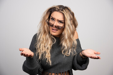 Young woman in eyeglasses feeling puzzled on gray background