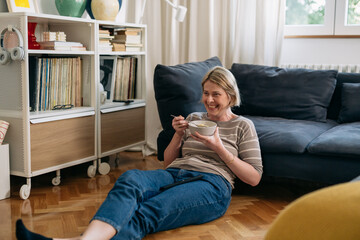 woman having cornflakes for breakfast and watching tv at home