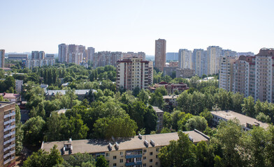 Fototapeta premium Panoramic top view - cityscape with modern buildings and lush tree foliage on a clear sunny summer day and blue sky