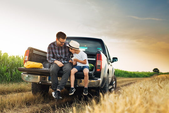 father and son sits on trunk of truck in wheat field