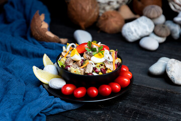 Fish salad with sardines, harringe, tuna, tomato, lemon, lettuce, cabbage, olives, beans, corn, carrotes and eggs on rustic kitchen table