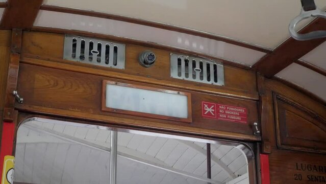 Lisbon historical cable tram next stop announcement sign flashing and safety handle swinging. Vintage transportation vehicle wooden interior. CCTV security camera and ventilation grills above sign.
