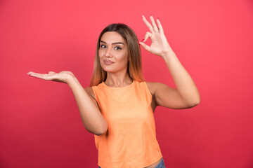 Pretty young woman making ok sign on red background