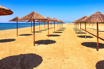 Row of wooden umbrellas at sandy beach, sea and blue sky vacation background, Greece