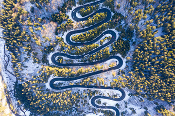 Aerial drone photograph bird's eye perspective of a beautiful winding mountain road in Romania in winter time - 515607563
