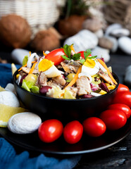 Fish salad with sardines, harringe, tuna, tomato, lemon, lettuce, cabbage, olives, beans, corn, carrotes and eggs on rustic kitchen table