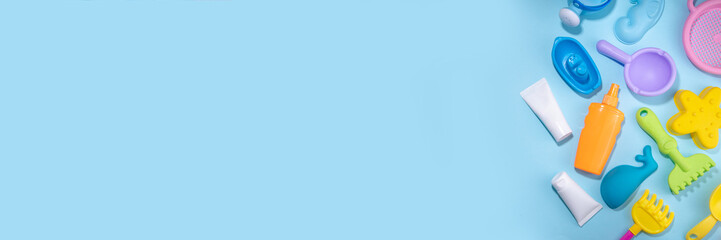 Baby Sunscreen suncare concept. Suntan lotion bottles with kids vacation accessory, sand molds, panama hat, on light blue background copy space