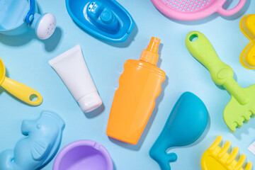 Fototapeta premium Baby Sunscreen suncare concept. Suntan lotion bottles with kids vacation accessory, sand molds, panama hat, on light blue background copy space