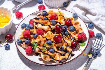 Sweet waffles with berry. Homemade summer breakfast belgian waffles with raspberries, blueberries, strawberry honey and chocolate dip sauce, copy space