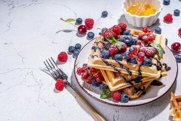 Sweet waffles with berry. Homemade summer breakfast belgian waffles with raspberries, blueberries, strawberry honey and chocolate dip sauce, copy space