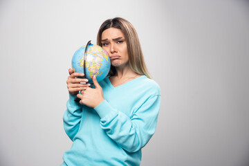 Blonde girl in blue sweatshirt holds a globe and looks uncertain and confused