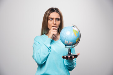 Blonde girl in blue sweatshirt holding a globe, thinking carefully and trying to remember