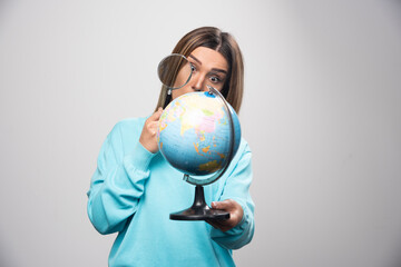 Fototapeta premium Blonde girl in blue sweatshirt holding a globe and looking for a destination with magnifier