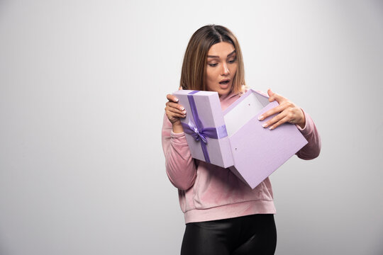 Blonde lady in pink sweatshirt opens up a gift box and gets surprized