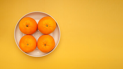 Top view of fresh oranges in a white dish over a yellow background