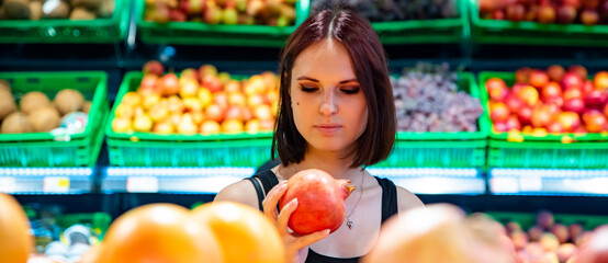 young woman in supermarket choosing pomegranate fruits