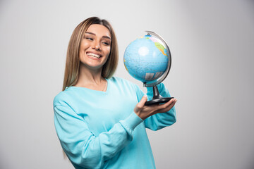 Fototapeta premium Blonde girl in blue sweatshirt holding a globe, guessing location and having fun