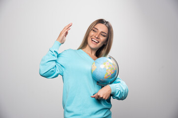 Blonde girl in blue sweatshirt holding a globe, guessing location and having fun