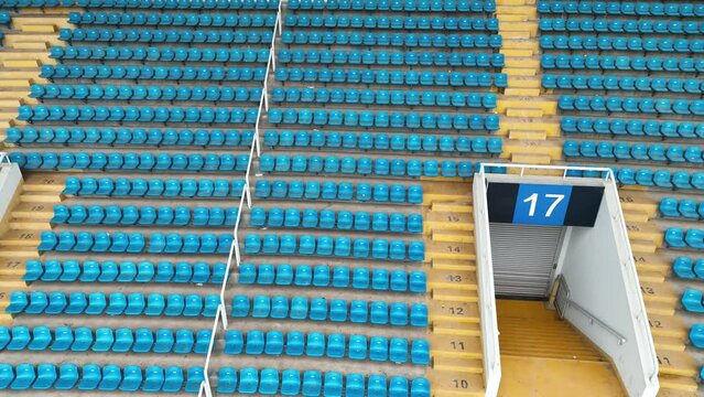 Empty audience seats in the giant stadium. Drone aerial view. Flying around empty stadium, blue audience auditorium inside during pandemic period.  Sports business and covid-19 concept b-roll footage.