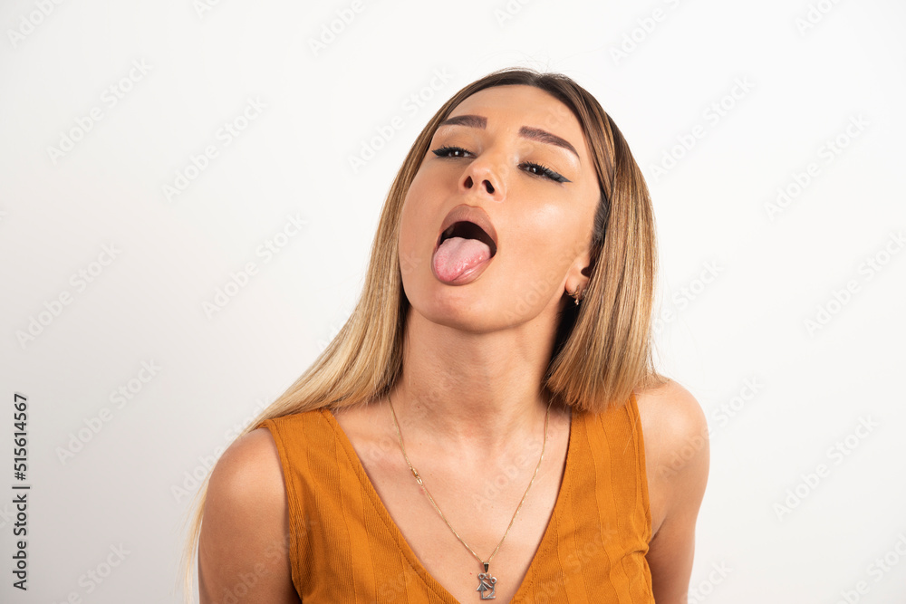 Wall mural Funny woman showing a tongue on white background