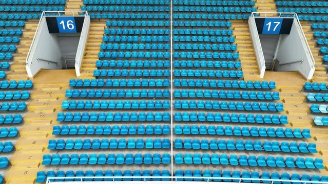 Empty audience seats in the giant stadium. Drone aerial view. Flying around empty stadium, blue audience auditorium inside during pandemic period.  Sports business and covid-19 concept b-roll footage.