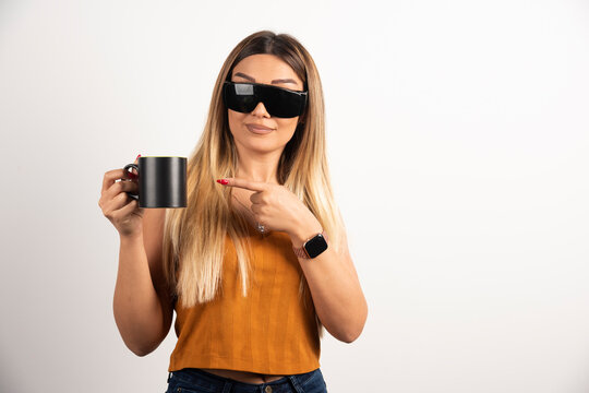 Young woman pointing at black cup and wearing goggles