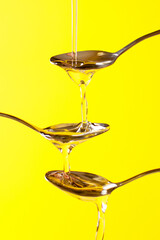 close up on spoons on which liquid honey is poured on a yellow background