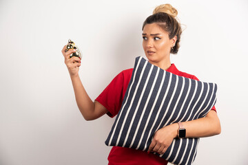 Young woman in red short showing an alarm clock and holding a pillow