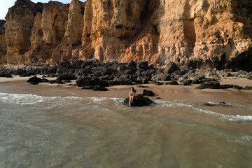Calm woman enjoying sunny day on sandy beach near cliffs