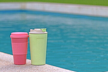 Obraz premium Two recyclable plastic cups next to a swimming pool