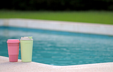 Fototapeta na wymiar Two recyclable plastic cups next to a swimming pool