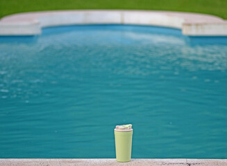 A recyclable plastic cup next to a swimming pool