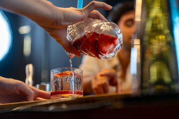 Professional male bartender preparing and serving cocktail drink to customer on bar counter at luxury nightclub. Barman making mixed alcoholic drink for celebrating holiday party at restaurant bar.