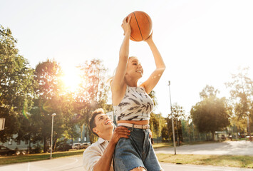 summer holidays, sport and people concept - happy young couple with ball playing on basketball playground