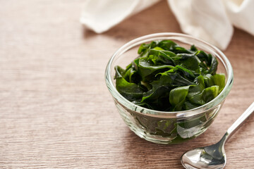 close up laminaria (Kelp) seaweed in glasses bowl and steel spoon on wooden table background with copy space                                                                                       