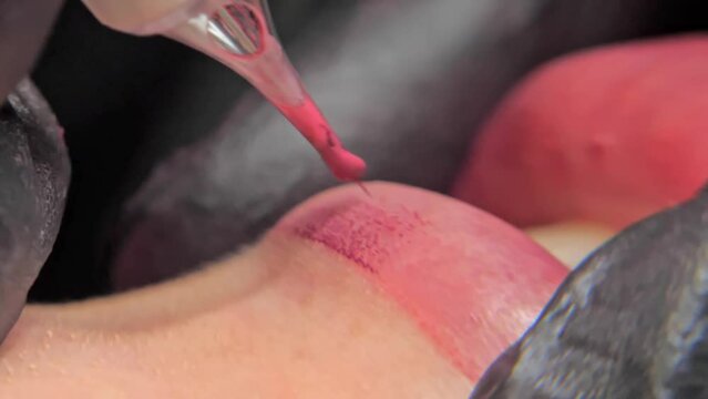Close-up of a permanent makeup procedure. A needle pierces the lips and injects paint under the skin. Macro