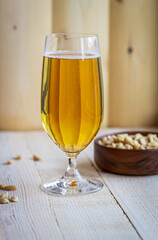A glass of the light beer on the wooden background with a cup of pistachios