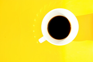 white cup of strong invigorating coffee on bright yellow morning background under sunlight with shadows and glare. Top view, flat lay