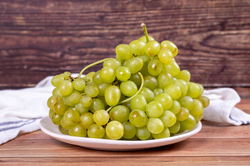 Fresh green grapes. Ripe grapes in plate on wood background. Bulk grapes. close up